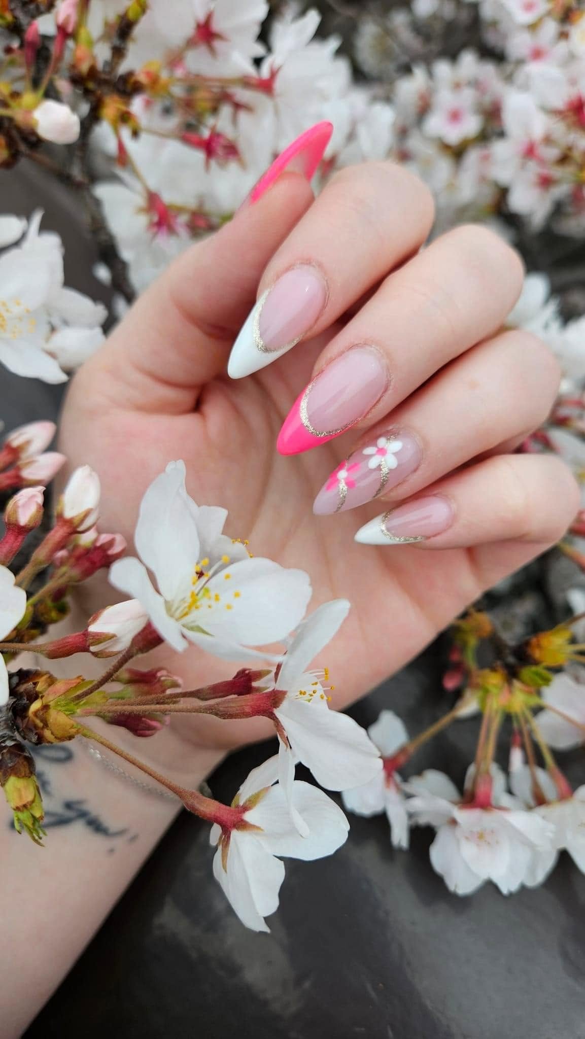 Almond-shaped French manicure with pink and white floral nail art by Pleasant Nails & Spa in Grand Rapids, photographed against cherry blossoms